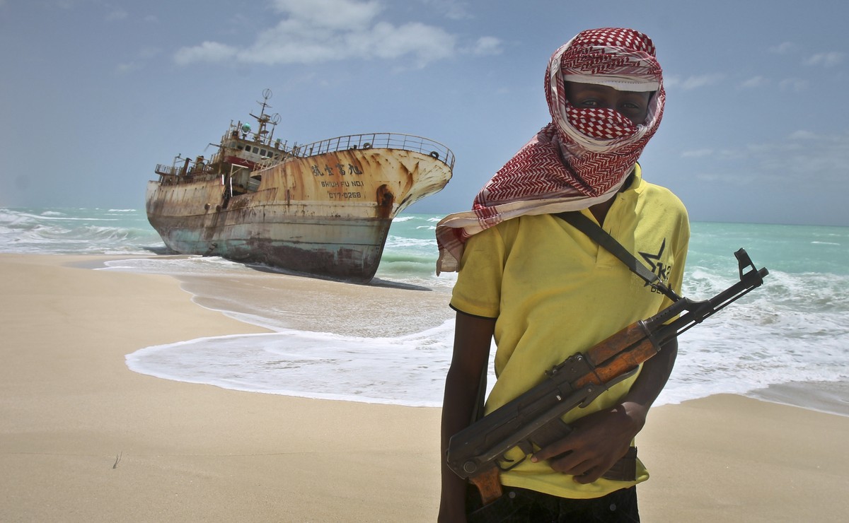 FILE - In this Sunday, Sept. 23, 2012 file photo, masked Somali pirate Hassan stands near a Taiwanese fishing vessel that washed up on shore after the pirates were paid a ransom and released the crew, ...