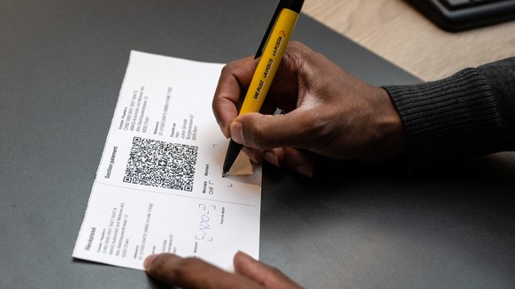Ein Mitarbeiter der Post fuellt einen Einzahlungsschein mit QR Code aus, am Mittwoch, 28. September 2022, in einer Postfiliale in Bern. Die rosa und orangen Einzahlungsscheine werden per 1. Oktober mi ...