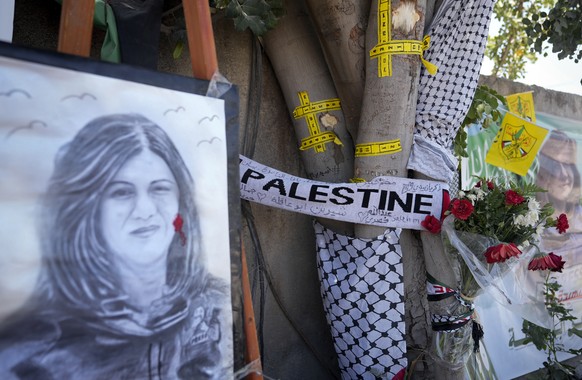 FILE - Yellow tape marks bullet holes on a tree and a portrait and flowers create a makeshift memorial, at the site where Palestinian-American Al-Jazeera journalist Shireen Abu Akleh was shot and kill ...