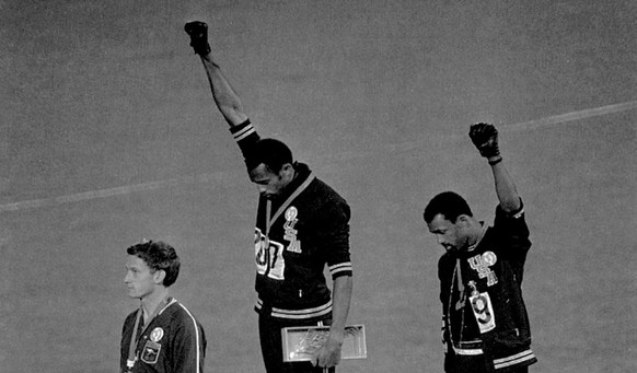 Extending gloved hands skyward in racial protest, U.S. athletes Tommie Smith, center, and John Carlos, stare downward October16, 1968 during the playing of the Star Spangled Banner after Smith receive ...