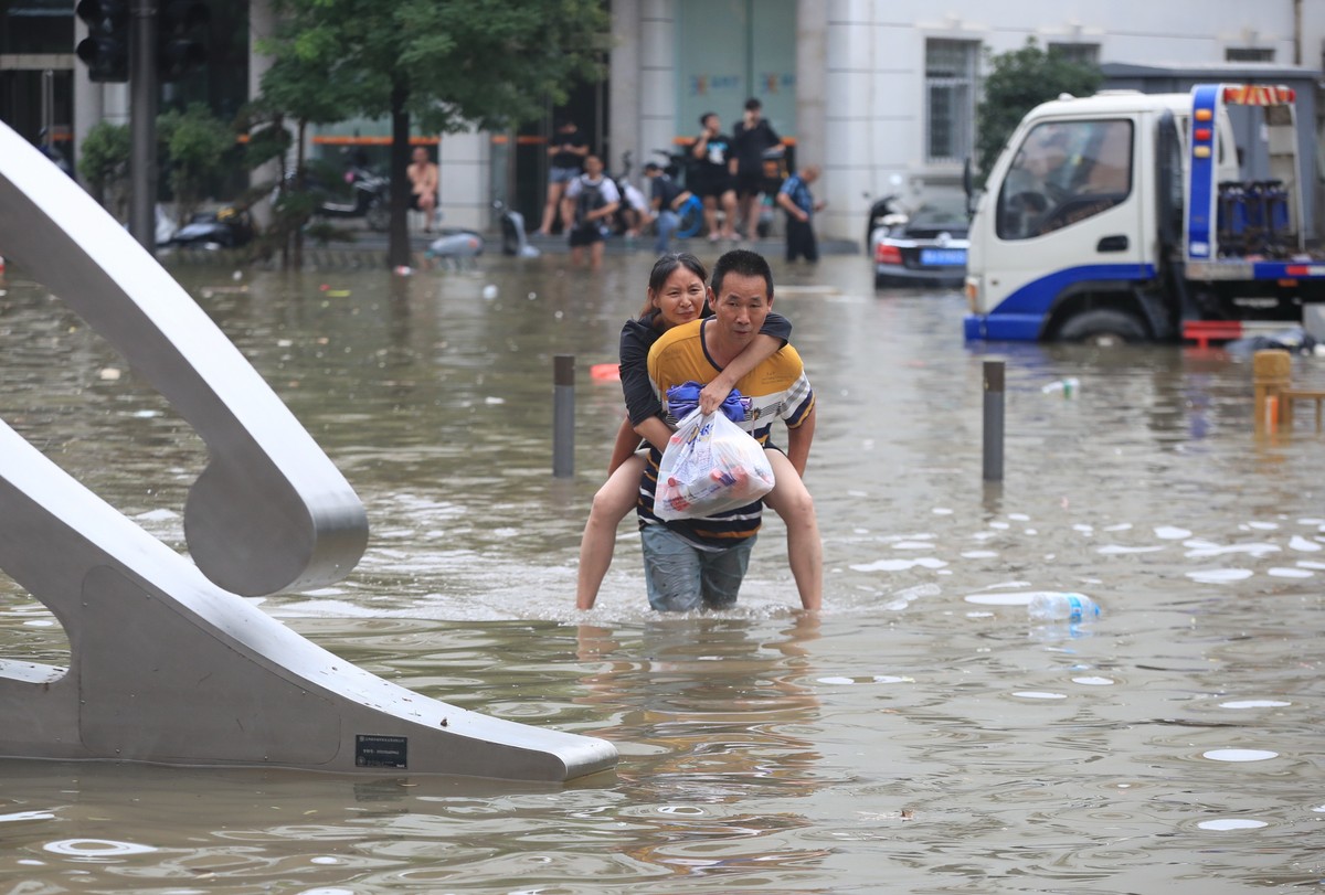 epa09356173 A man carries a woman in the flooded road after record downpours receded in Zhengzhou city in central China's Henan province, 21 July 2021. Heavy floods in Central China killed 12 in  ...