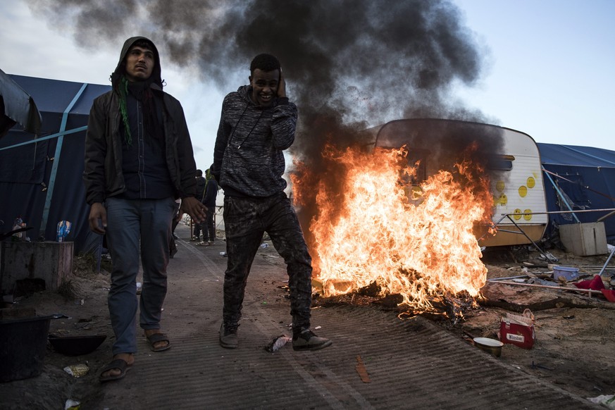 epa05602591 Migrants walk next to a fire caused by other migrants setting alight some of their belongings, as workers dismantle the makeshift camp &#039;the Jungle&#039; during its evacuation in Calai ...