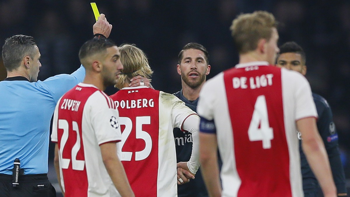 This Wednesday Feb. 13, 2019, image shows referee Damir Skomina, left, showing a yellow card to Real's Sergio Ramos, center, after a foul on Ajax's Kasper Dolberg during the first leg, round ...