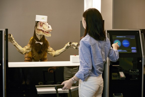 epa04848621 An undated handout image provided by amusement park operator Huis Ten Bosch Co., Ltd. shows a woman standing before a receptionist dinosaur robot at the â€˜Henn na Hotelâ€™ (or Weird Hotel ...