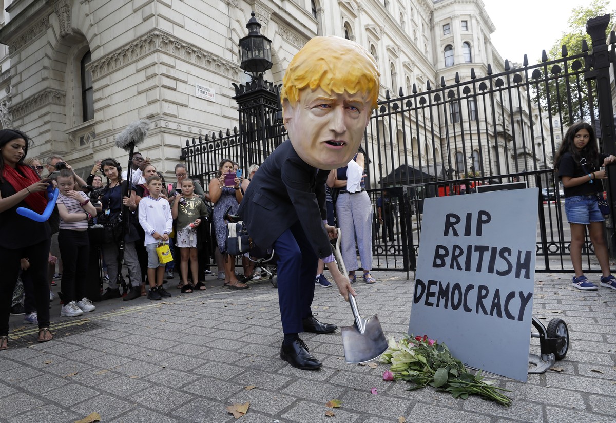 A man in a giant Boris Johnson 'head' digs a grave at the foot of a pretend tombstone outside Downing Street in London, Wednesday, Aug. 28, 2019. Britain's Queen Elizabeth II has approv ...