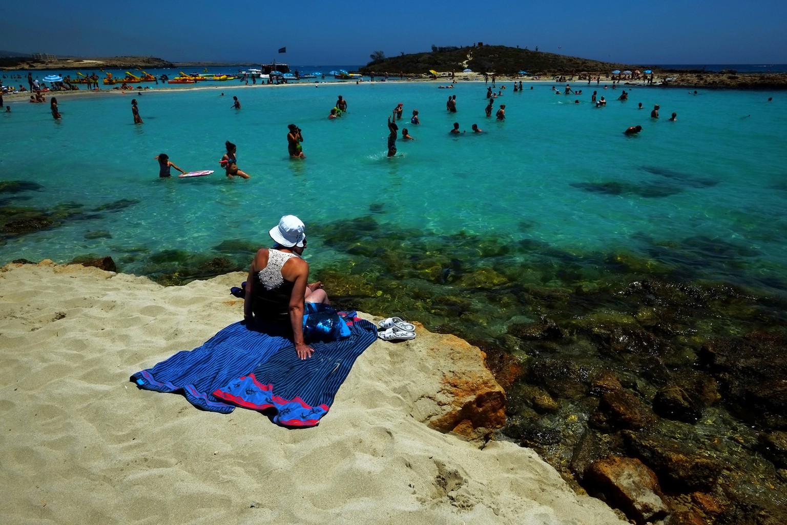 A woman sit on the sand as other people enjoy the sea at &quot;Nissi Beach&quot; in the famous southeastern coastal resort of Ayia Napa, Cyprus, Saturday, June 14, 2014. Some 2. 4 million tourists vis ...
