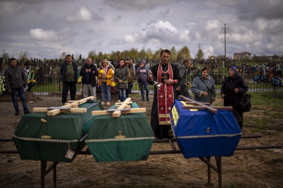 A priest blesses the remains of three people who died during the Russian occupation and were disinterred from temporary burial sites in Bucha, on the outskirts of Kyiv, on Wednesday, April 27, 2022. ( ...
