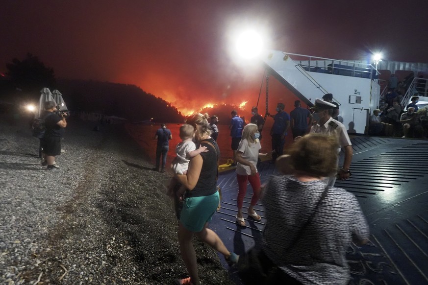People embark a ferry during an evacuation from Kochyli beach as wildfire approaches near Limni village on the island of Evia, about 160 kilometers (100 miles) north of Athens, Greece, Friday, Aug. 6, ...