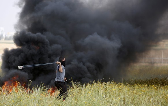 A Palestinian protester slings stones towards Israeli soldiers during clashes with Israeli troops along the Gaza Strip border with Israel, east of Khan Younis, Gaza Strip, Friday, March 30, 2018. (AP  ...