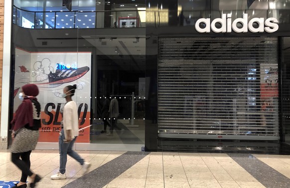 epa08869111 A picture taken by a mobile-phone shows women pass by a closed branch of German sportswear company Adidas in Beirut, Lebanon, 07 December 2020. Adidas will close down its branches includin ...