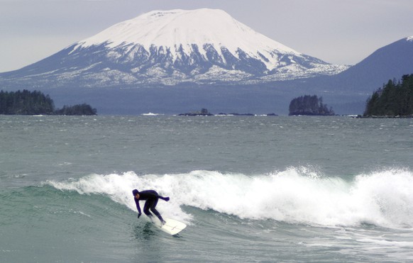 FILE - With Mount Edgecumbe in the background, Martha Robertson surfs at Sandy Beach in Sitka, Alaska, on Dec. 4, 2003. A swarm of hundreds of small earthquakes have been reported near Mount Edgecumbe ...