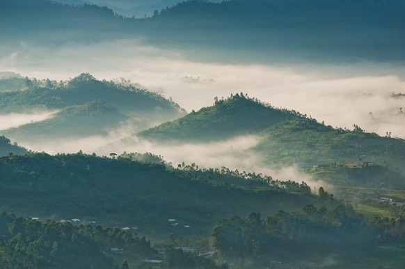 Houses in a small village are dwarfed by the looming presence of a volcanic mountain, Rwanda,