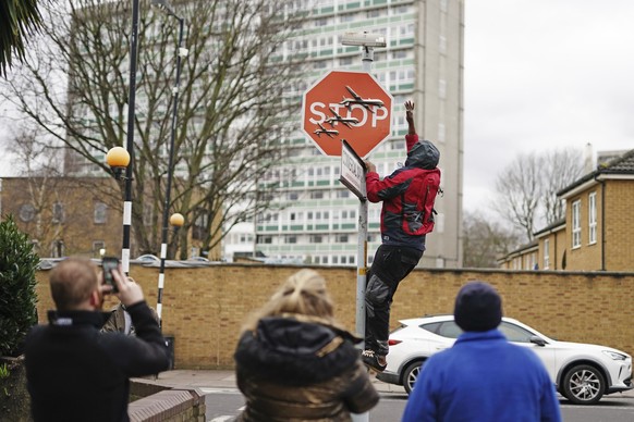 A person removes a Banksy artwork showing what appears to be three drones on a traffic stop sign, which was unveiled at the intersection of Southampton Way and Commercial Way in Peckham...