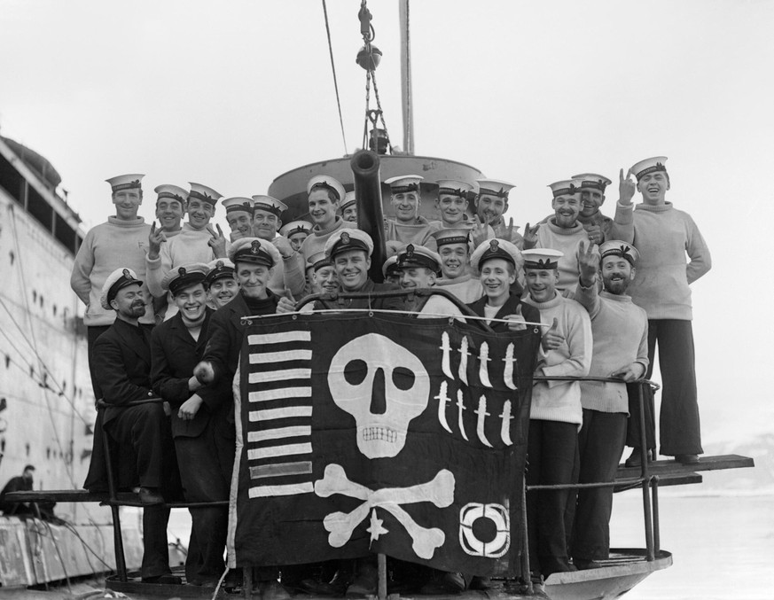 The personnel of the British submarine HMS Utmost showing off their Jolly Roger in February 1942. The markings on the flag indicate the boat&#039;s achievements: nine ships torpedoed (including one wa ...
