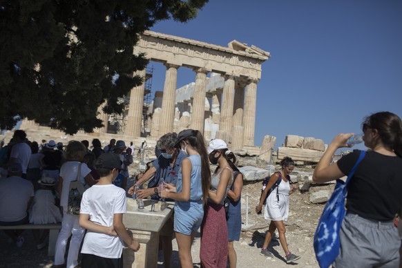 Tourists fill up their water bottles, in front of the ancient temple of Parthenon at Acropolis Hill, in Athens, Friday, July 31, 2020. Greece cautiously reopened its tourism industry, despite tough new coronavirus restrictions that came into force this week. Most of the new restrictions are unrelated to tourism. (AP Photo/Petros Giannakouris)