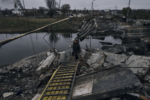 A woman walks across an exploded bridge in Bakhmut, Ukraine, Donetsk region, Ukraine, Friday, Nov. 11, 2022. (AP Photo/LIBKOS)
