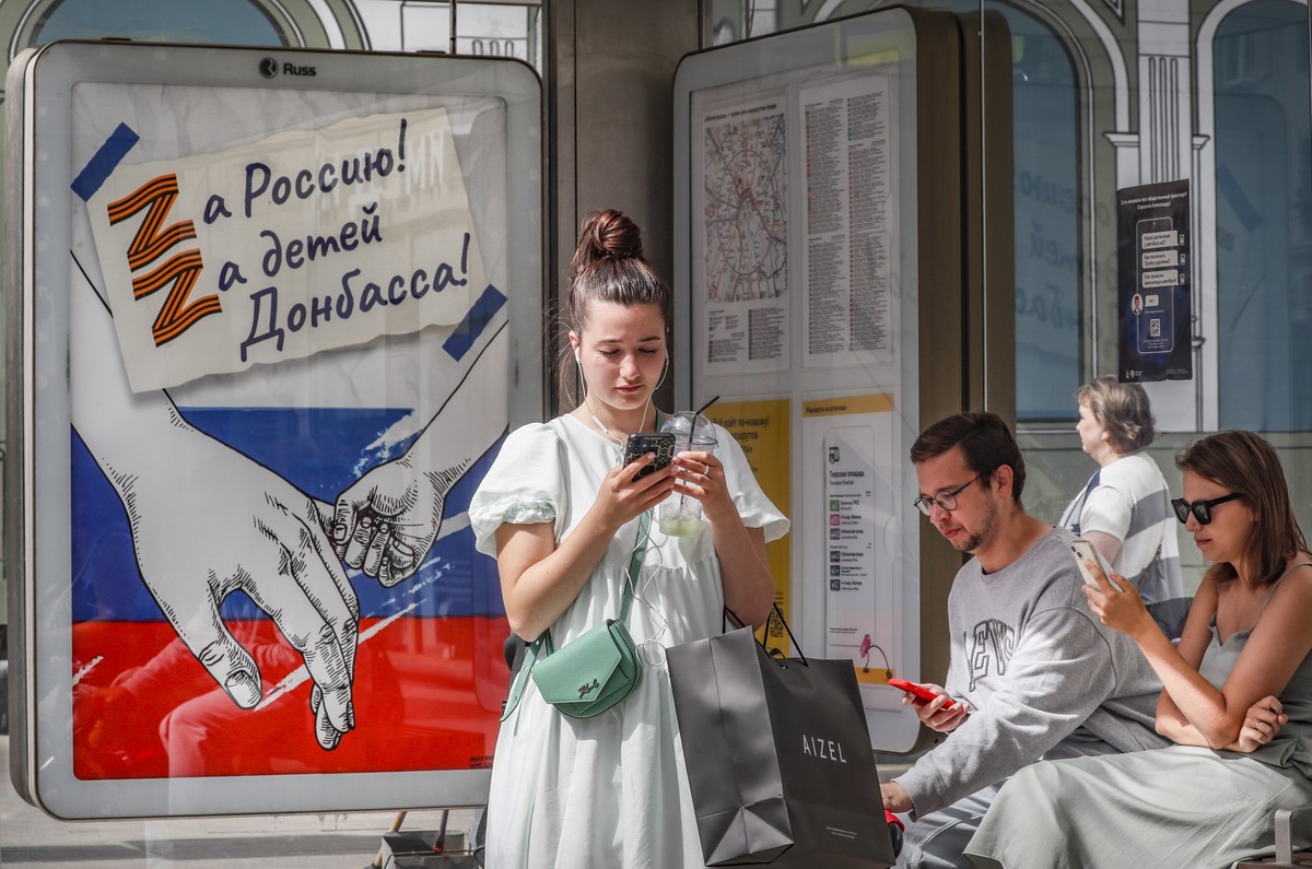 epa10072821 People wait at a bus stop featuring a poster with the inscription 'For Russia, For the children of Donbass' in Moscow, Russia, 15 July 2022. On 24 February Russian troops invaded ...