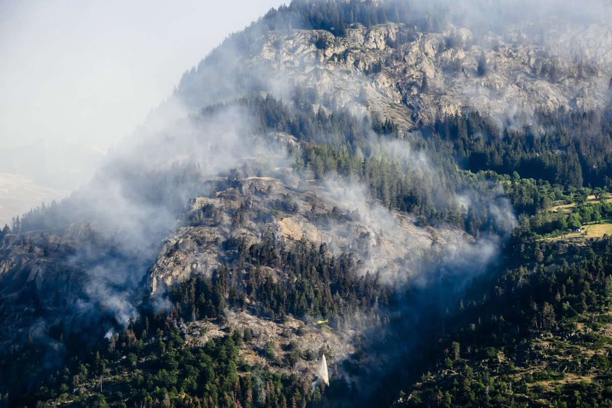 Un helicoptere verse de l'eau sur la fumee qui s'echappe de la foret en feu au dessus des communes de Bitsch et Ried-Moerel le mardi 18 juillet 2023 depuis Termen. Les h