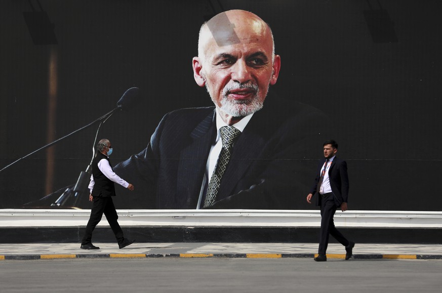 People walk near a mural of President Ashraf Ghani at Hamid Karzai International Airport, in Kabul, Afghanistan, Saturday, Aug. 14, 2021. As a Taliban offensive encircles the Afghan capital, there&#03 ...