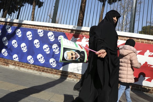 A mourner holds a poster of Iranian Gen. Qassem Soleimani, as she walks back from a funeral ceremony for him and his comrades, who were killed in Iraq in a U.S. drone attack on Friday, passing a satir ...