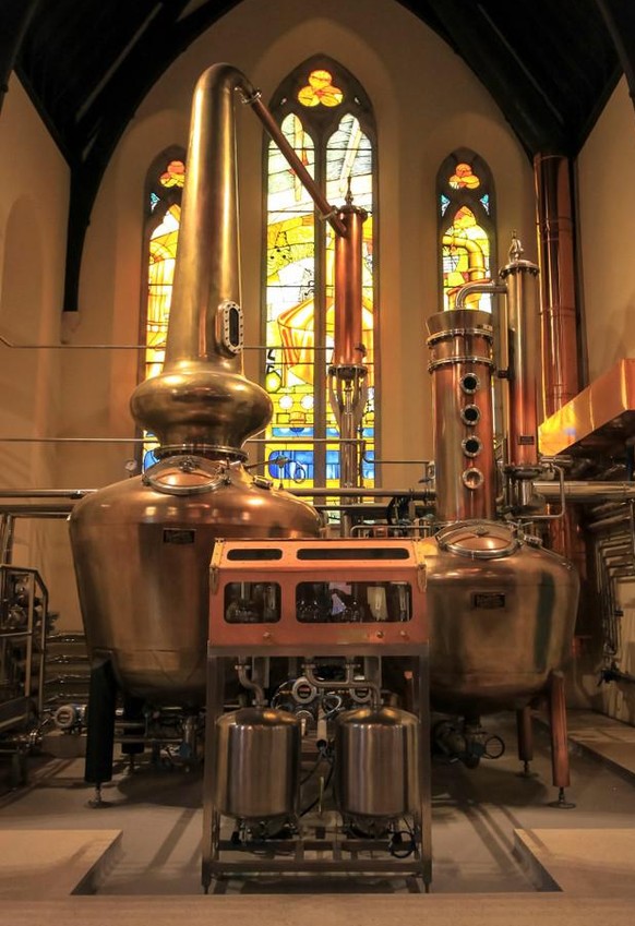 DUBLIN, IRELAND. OCTOBER 03, 2018. Pot Still equipment at the altar of an St James Church, with stained glass in the background, at Pearse Lyons Distillery.