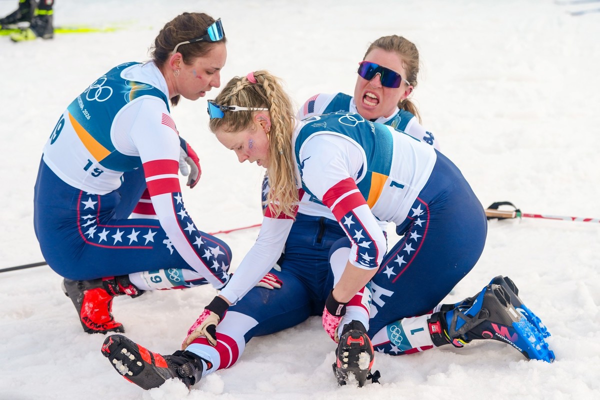 Jessie Diggins and Julia Kern, left, of the United States, help teammate Rosie Brennan suffering from cramps after crossing the finish line in the cross country skiing women's 10km + 10km skiathl ...