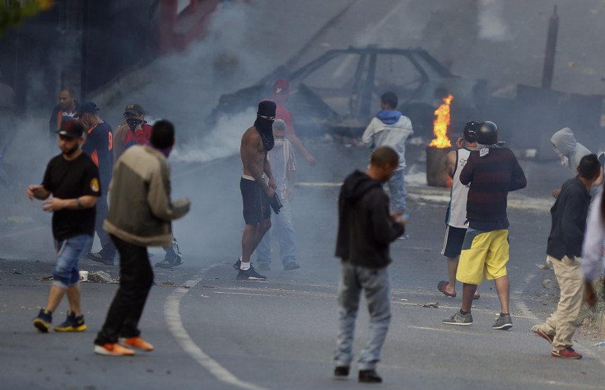Anti-government protesters stand amid tear gas as they face off with security forces and protest in support of an apparent mutiny by a national guard unit in the Cotiza neighborhood of Caracas, Venezu ...