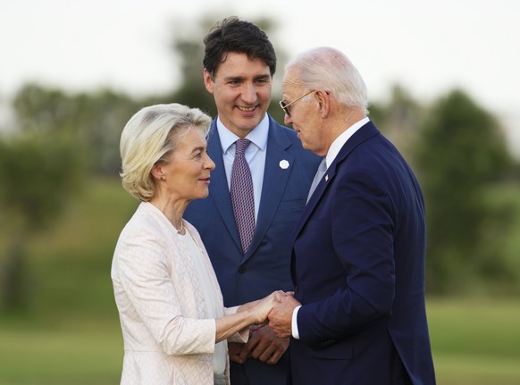 FILE -Canadian Prime Minister Justin Trudeau, middle, President of the European Commission Ursula von der Leyen, left, and U.S. President Joe Biden talk as they wait for the start of a skydiving exhib ...
