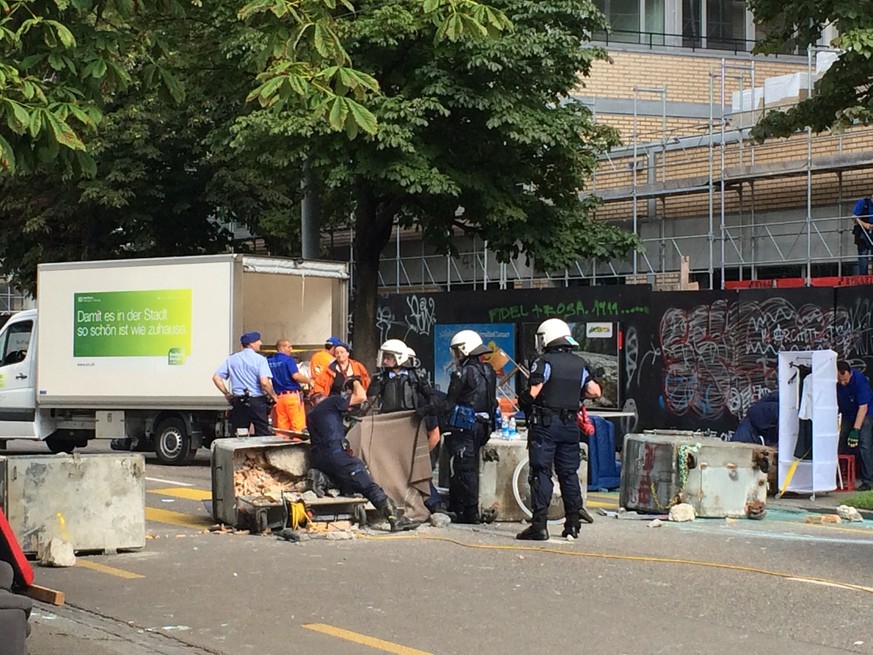 Zürcher Stadtpolizisten sägen die Ketten eines an Containern befestigten Strassenblockierers auf.