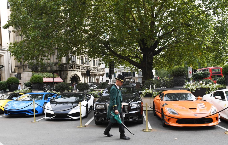epa06984357 A doorman uses a leaf blower to clean the space in front of super cars parked outside a hotel in Park Lane in London, Britain, 30 August 2018. August in known as the &#039;Super Car Season ...