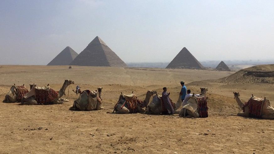 FILE - In this Aug. 30, 2015, file photo, camels rest between rides with their owners against the backdrop of the pyramids in Giza, Egypt. Archaeologists in Egypt say they have discovered a 4,400-year ...