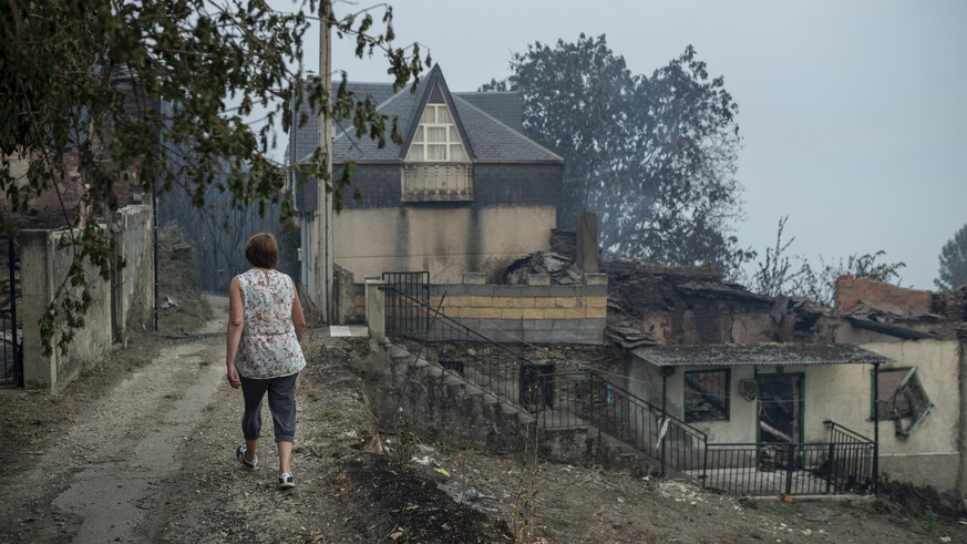 epa10077295 A resident walks past a burnt house in the village of Alixo, O Barco de Valdeorras, Galicia, northwestern Spain, 18 July 2022. The forest fire has destroyed at least six houses and more th ...