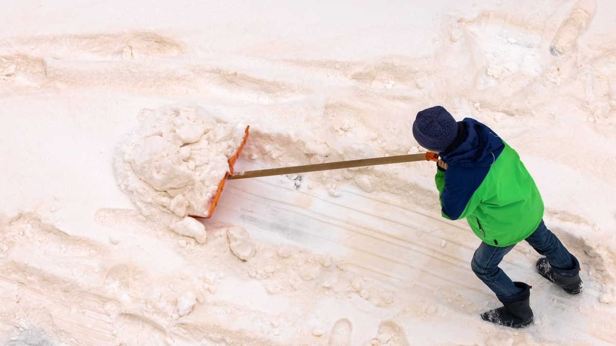 Blutschnee mit Sandstaub aus der Sahara Ein Kind schiebt mit einem Schneeschieber eine Spur in den in Schichten gef