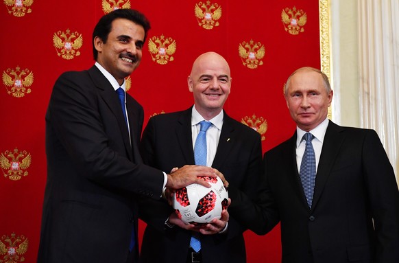 epa06889816 Emir of Qatar Sheikh Tamim bin Hamad Al Thani (L), Russian President Vladimir Putin (R) and FIFA President Gianni Infantino (C) pose with a ball during a symbolic ceremony of transferring  ...