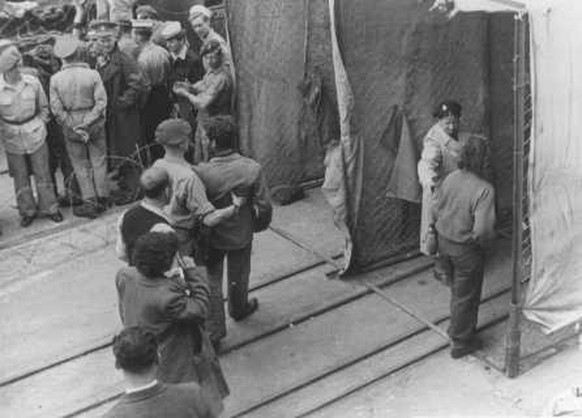 Britische Soldaten zwingen jüdische Flüchtlinge vom Schiff <em>Theodor Herzl</em> durch eine Desinfektionsstation, bevor sie in Internierungslager auf Zypern deportiert werden, im Hafen von Haifa, Palästina, 24. April 1947.