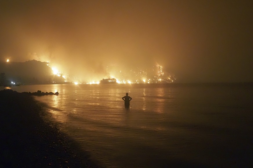 A man watches the flames as wildfire approaches Kochyli beach near Limni village on the island of Evia, about 160 kilometers (100 miles) north of Athens, Greece, late Friday, Aug. 6, 2021. Wildfires r ...