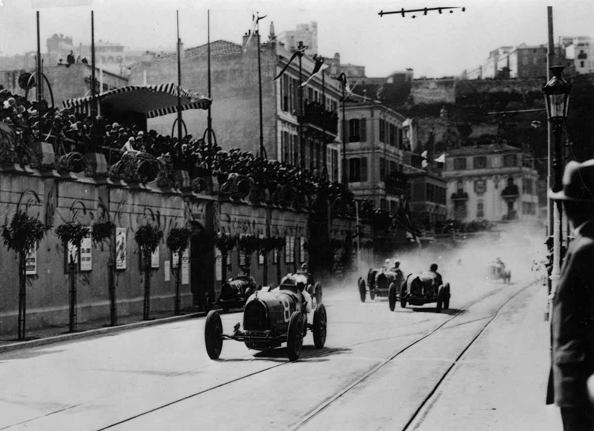 Start of the inaugural Monaco Grand Prix, 1929. Crowds watch as the cars speed along the street, led by a Bugatti. Note the tramlines. This first running of the event was won by 'W Williams' ...