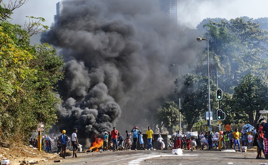 Looters outside a shopping centre alongside a burning barricade in Durban, South Africa, Monday July 12, 2021. Police say six people are dead and more than 200 have been arrested amid escalating viole ...