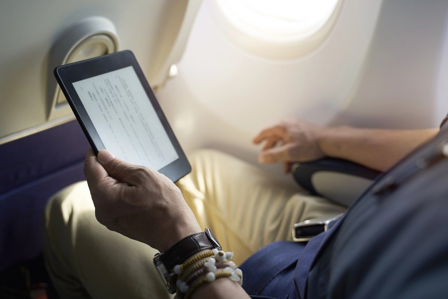 Asian man male passenger sitting in cabin of airplane reading ebook using e-reader model released