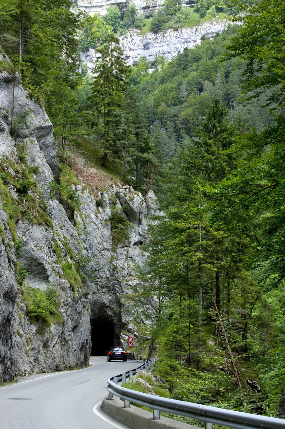 On the road that follows the creek "La Sorne", a car is about to disappear in a tunnel underneath the "Les Rochers Bacon" cliffs near Undervelier in the canton of Jura, Switzerland ...
