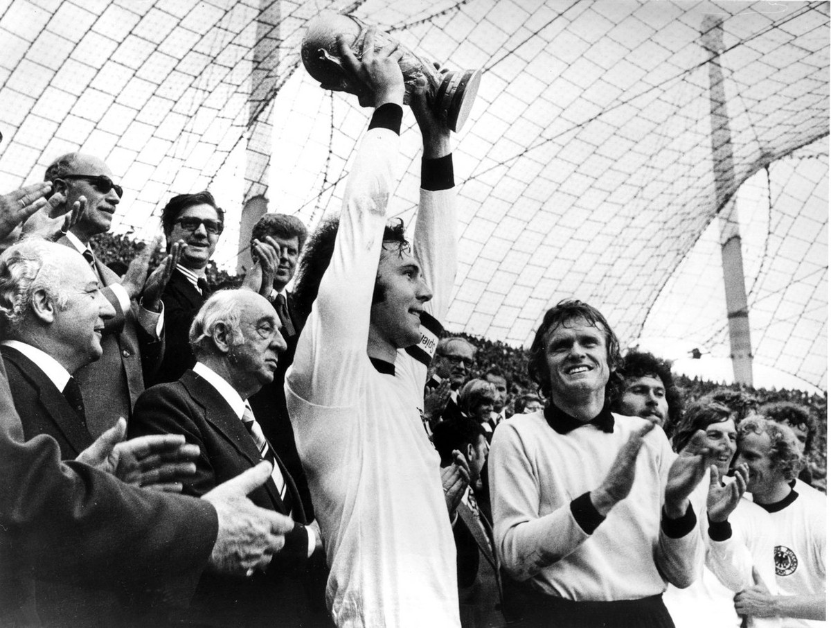 Franz Beckenbauer mit dem Weltmeisterpokal am 28.Mai 1974 im Muenchener Olympia-Stadion. V.l. Alt-Bundespraesident Walter Scheel, der damalige DFB-Chef Hermann Goesmann, rechts Sepp Maier, Paul Breitn ...