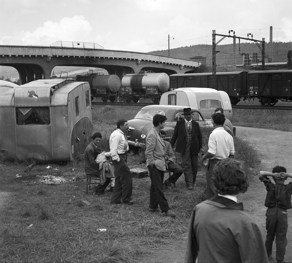 Am Stadtrand von Zuerich haben Fahrende einen Standplatz neben den Bahngeleisen, aufgenommen im Jahr 1958. Maenner stehen ihren Wohnwagen zum Gespraech im Kreis. (KEYSTONE/Str)