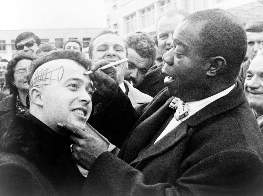 Louis Armstrong (1901-1971), African American Jazz musician, drawing a trumpet and autographing the side of a young man s head in Nice, France. 1960