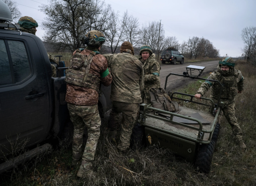 An der Front im Donetsk hat soeben eine ferngesteuerte Bodendrohne einen Verwundeten geborgen; dieser wird nun von Kameraden auf einen Pickup-Truck umgeladen.