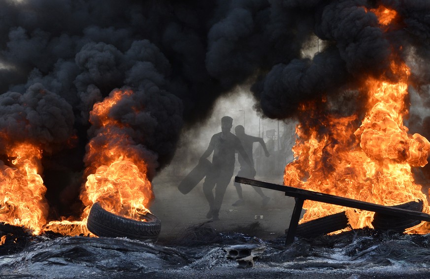 epa07929686 A protester throws a tire on a fire to block a Metn highway during a protest in north of Beirut, Lebanon, 18 October 2019. Protesters, mainly civil activists, started to demonstrate in dow ...