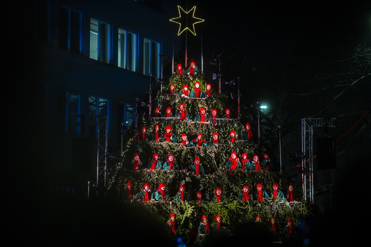 KEYPIX - Kinder mit roten Muetzen singen beim Singing Christmas Tree, auf einer eines Weihnachtsbaumes nachgebildeten Buehne aus Tannenaesten beim Werdmuehleplatz, am Dienstag, 9. Dezember 2025 in Zue ...