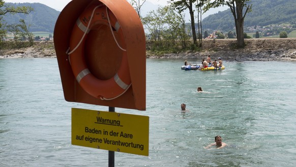 Aareschwimmer und Schlauchbootfahrer geniessen den schoenen Sommertag neben einem Rettungsring und einem Warnschild mit der Aufschrift &quot;Warnung - Baden in der Aare auf eigene Verantwortung&quot;  ...