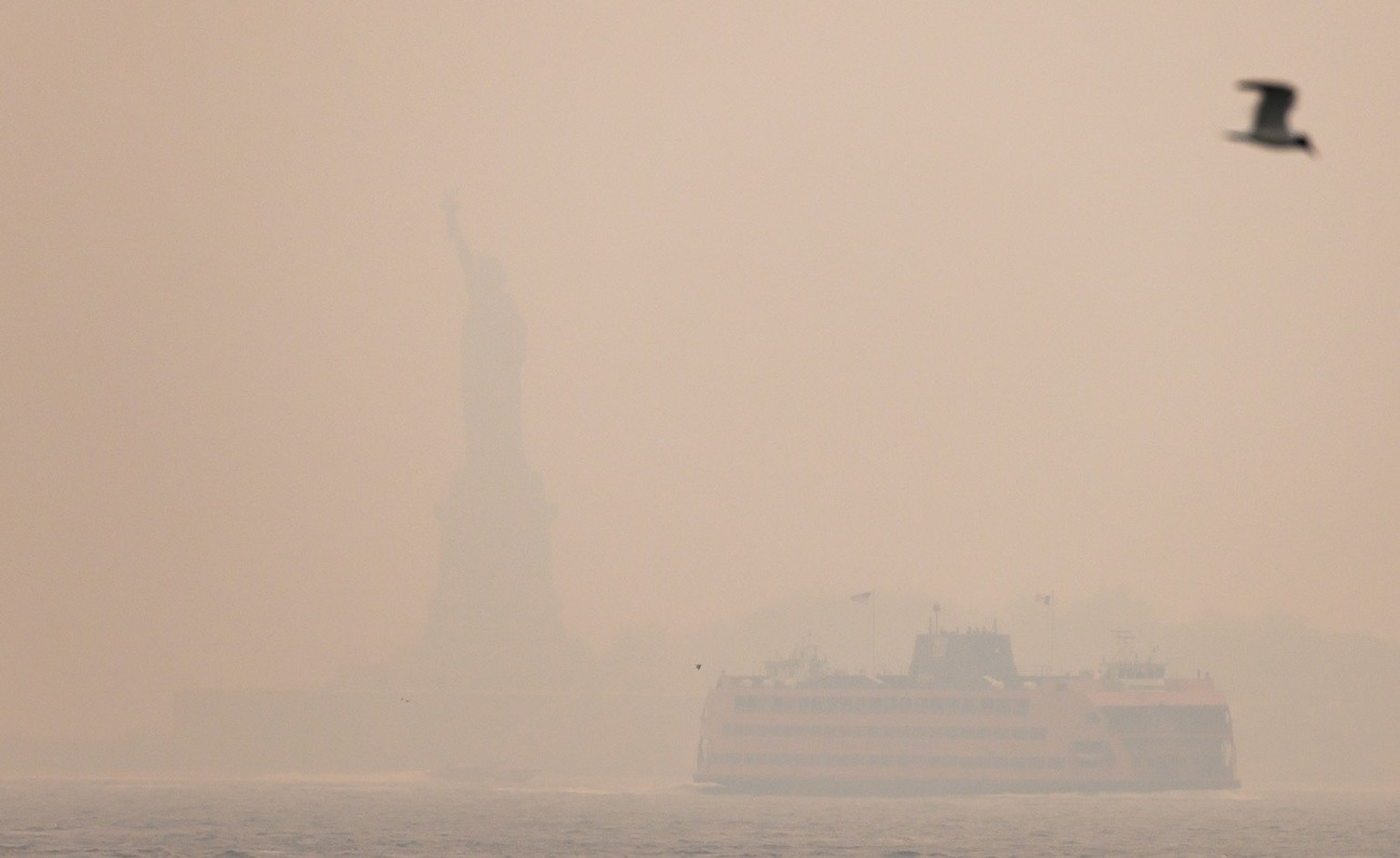 epa10678570 The Statue of Liberty and the Staten Island Ferry are obscured by smoke from wildfires burning in Canada over Manhattan in New York, New York, USA, 07 June 2023. All of New York City is un ...