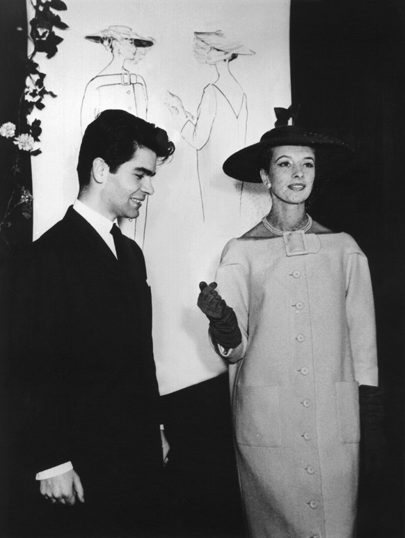 ARCHIV - 30.11.1953, ---: Der erst 16-jährige (nach anderen Angaben 21-jährige) Hamburger Mode-Student Karl Lagerfeld 1954 mit einem Model beim Vorführen des Cocktail-Mantels. Im Hintergrund seine Mod ...