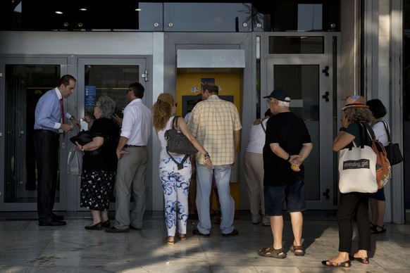 An elderly woman asks a question to a bank employee as people line up to an ATM machine outside the bank in Athens, on Monday, July 6, 2015. GreeceÂs Finance Minister Yanis Varoufakis has resigned fo ...